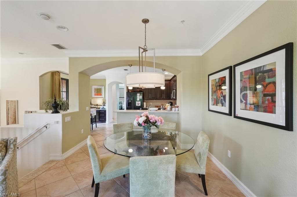 Dining space with light tile patterned floors, arched walkways, ornamental molding, and visible vents