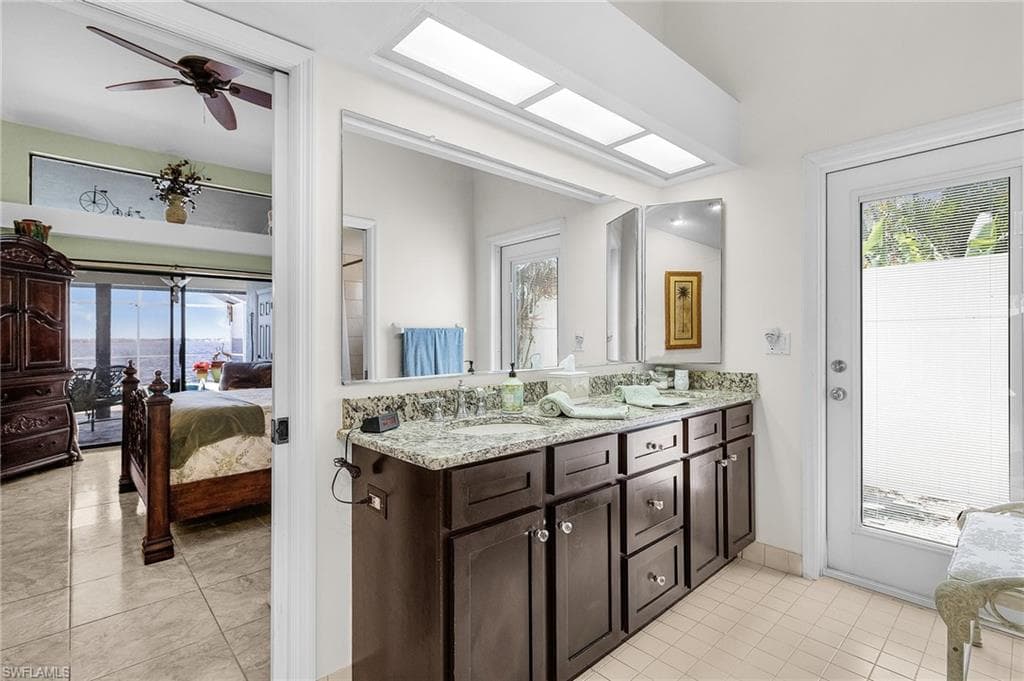 Primary ensuite Bathroom downstairs featuring tile patterned flooring, double vanity, and exterior door to atrium and south side yard
