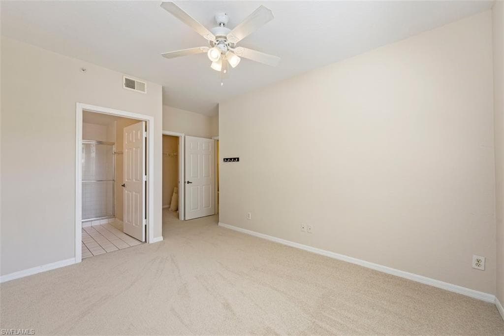 Unfurnished bedroom featuring light colored carpet, a spacious closet, a closet, ceiling fan, and ensuite bathroom