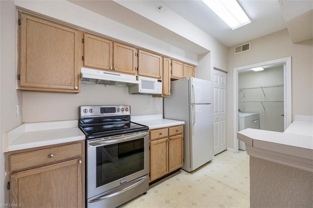 Kitchen with white appliances, washing machine and clothes dryer, under cabinet range hood, light floors, and light countertops