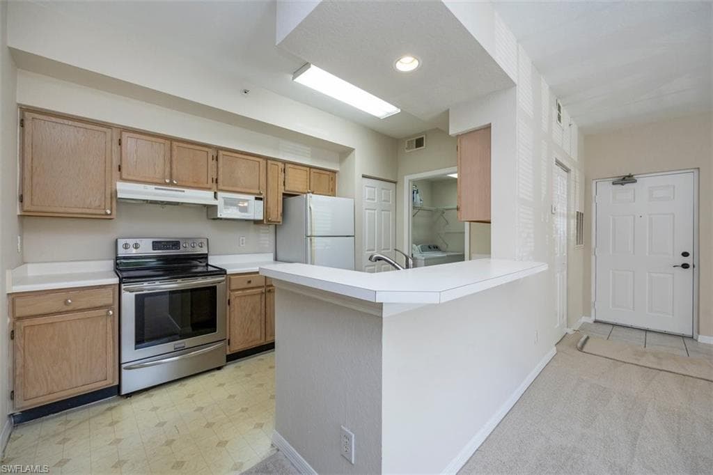 Kitchen with white appliances, under cabinet range hood, washing machine and dryer, light countertops, and recessed lighting