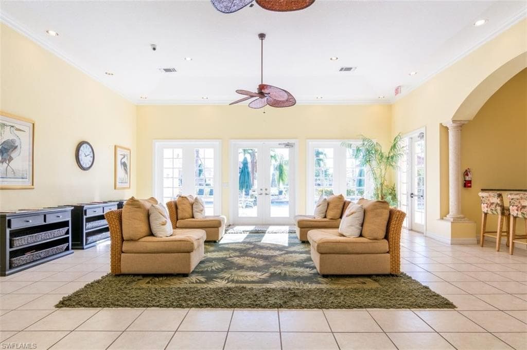 Living area featuring arched walkways, light tile patterned flooring, french doors, crown molding, and a ceiling fan