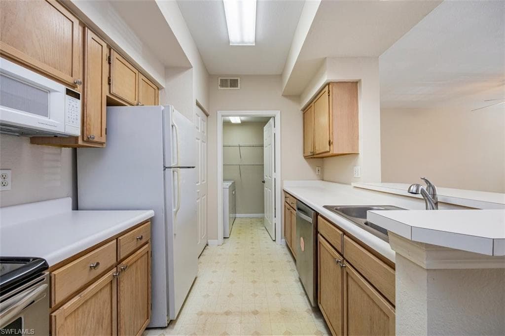 Kitchen with light flooring, white appliances, light countertops, a peninsula, and independent washer and dryer