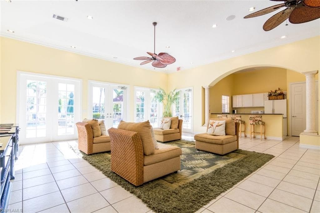 Living room with ceiling fan, light tile patterned flooring, arched walkways, french doors, and decorative columns