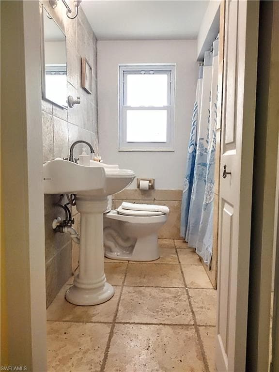 Bathroom featuring tile walls, toilet, and stone tile floors