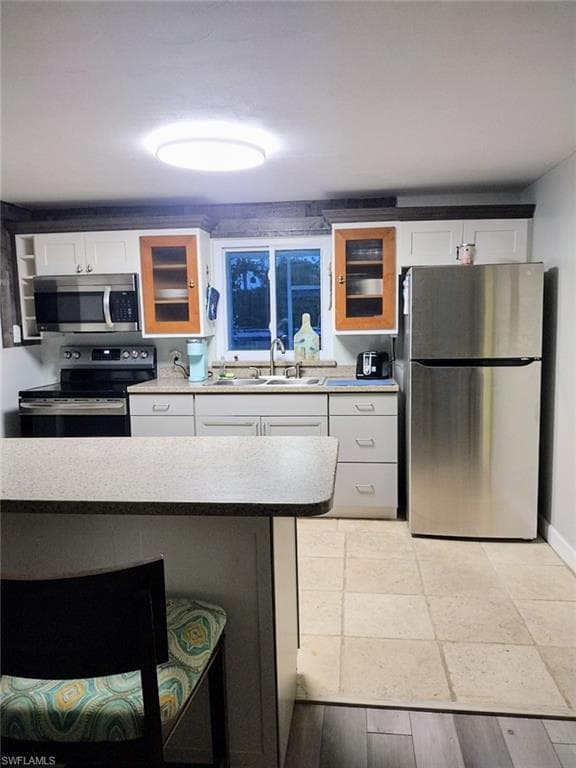 Kitchen featuring white cabinets, appliances with stainless steel finishes, a sink, and glass insert cabinets