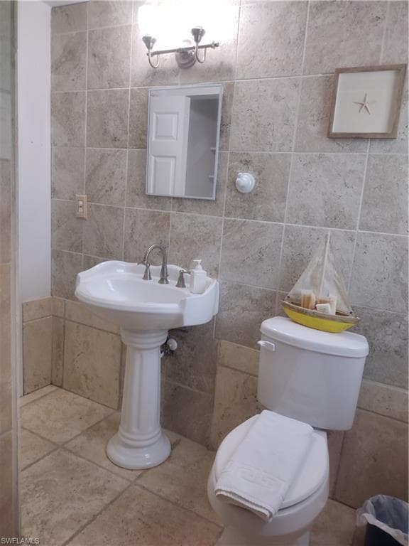 Half bathroom with toilet, tile walls, tile patterned flooring, and backsplash