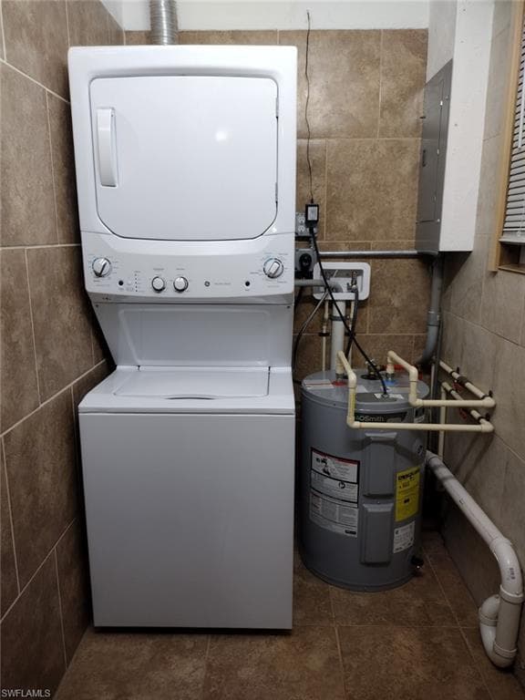 Washroom featuring water heater, tile walls, and stacked washer / drying machine