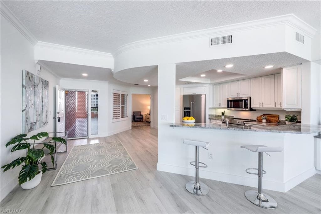 Kitchen featuring appliances with stainless steel finishes, light wood-style flooring, crown molding, a textured ceiling, and white cabinetry