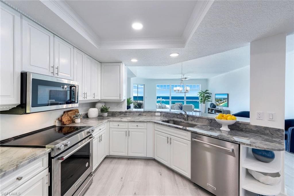 Kitchen featuring stainless steel appliances, a sink, a tray ceiling, crown molding, and a chandelier