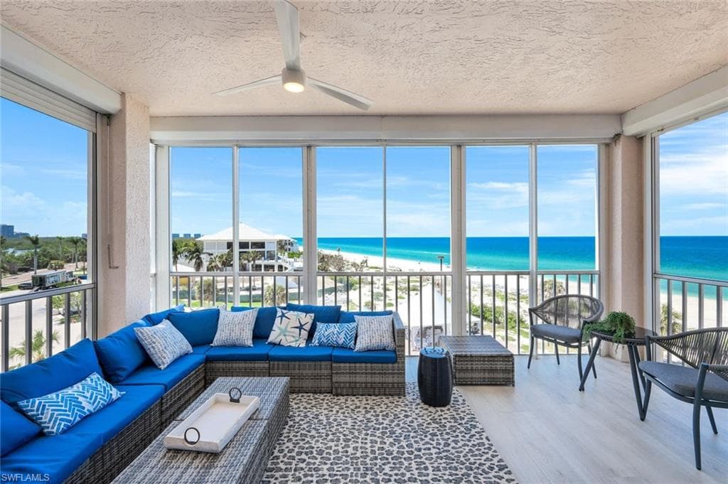 Sunroom with view of water and beach, wood finished floors, a textured ceiling, and healthy amount of natural light