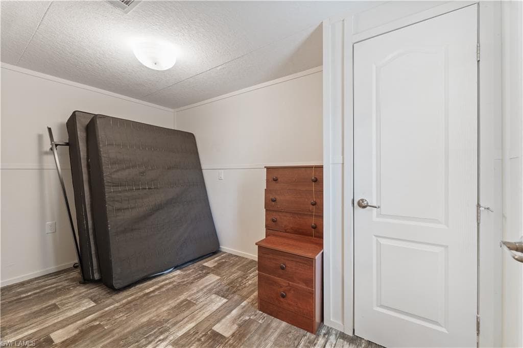 Bedroom with wood finished floors, a textured ceiling, and baseboards