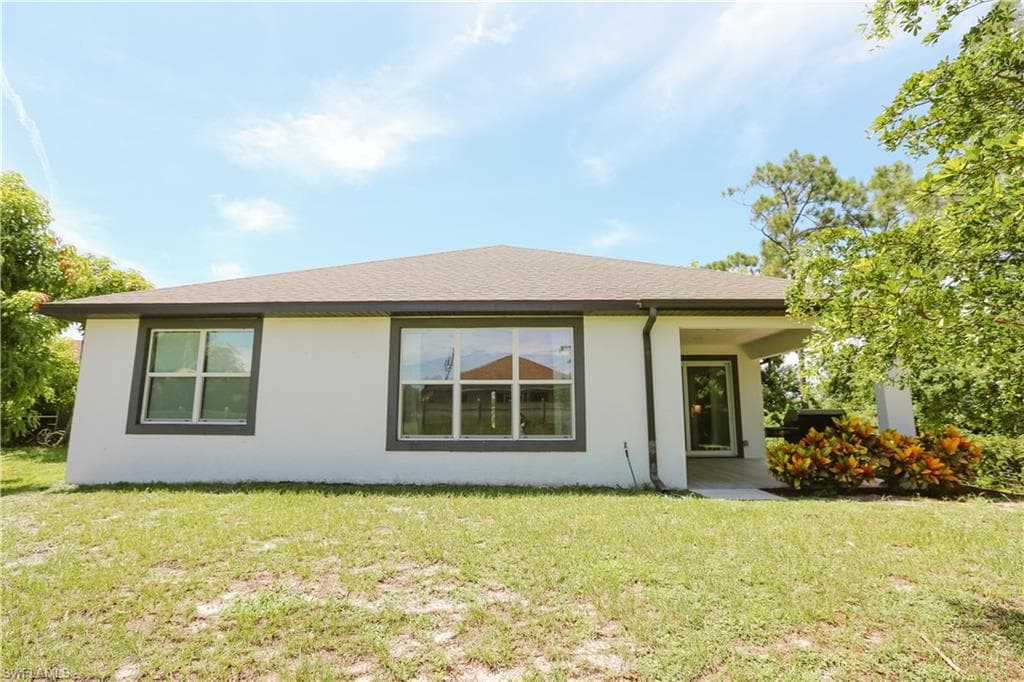Back of house featuring stucco siding and a lawn