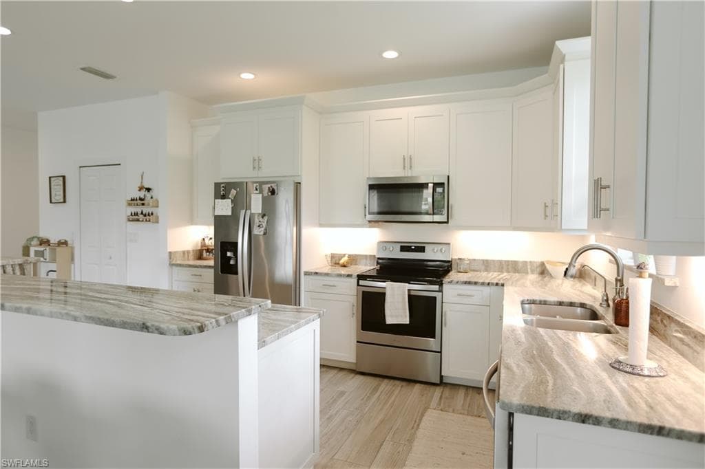 Kitchen with appliances with stainless steel finishes, a sink, light stone counters, white cabinets, and recessed lighting