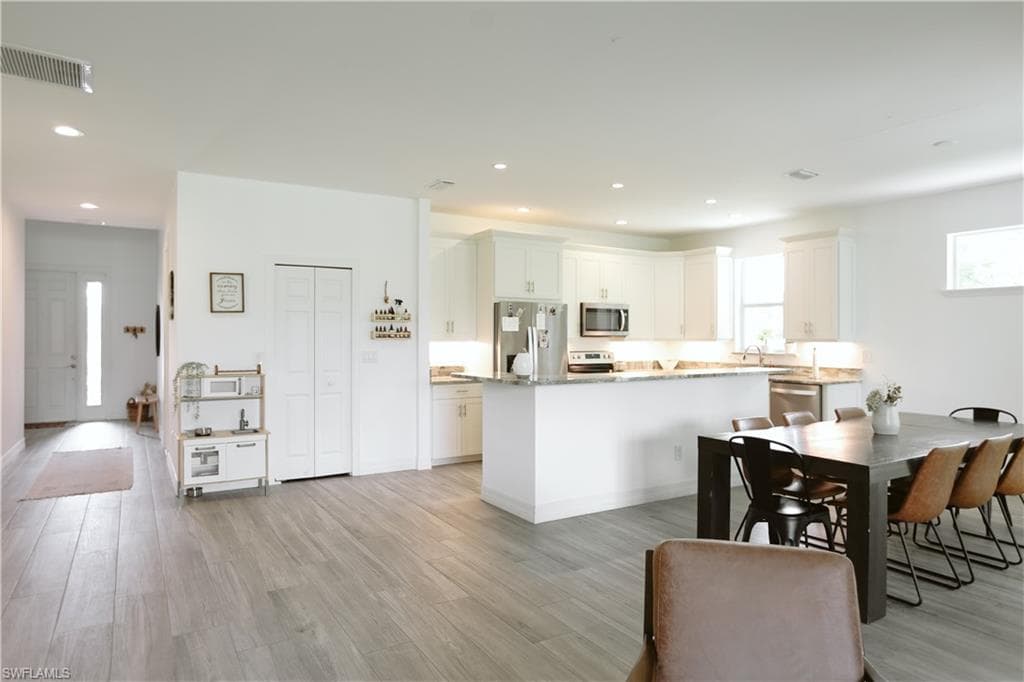 Kitchen with stainless steel appliances, light wood finished floors, a center island, recessed lighting, and white cabinets