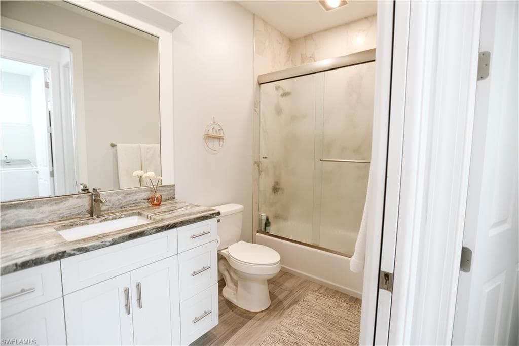 Full bath with vanity, toilet, shower / bath combination with glass door, and wood finished floors