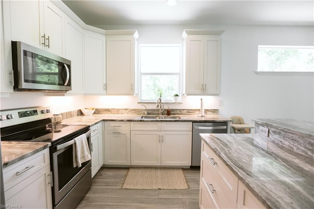 Kitchen with stainless steel appliances, a sink, light stone countertops, white cabinetry, and light wood-style floors