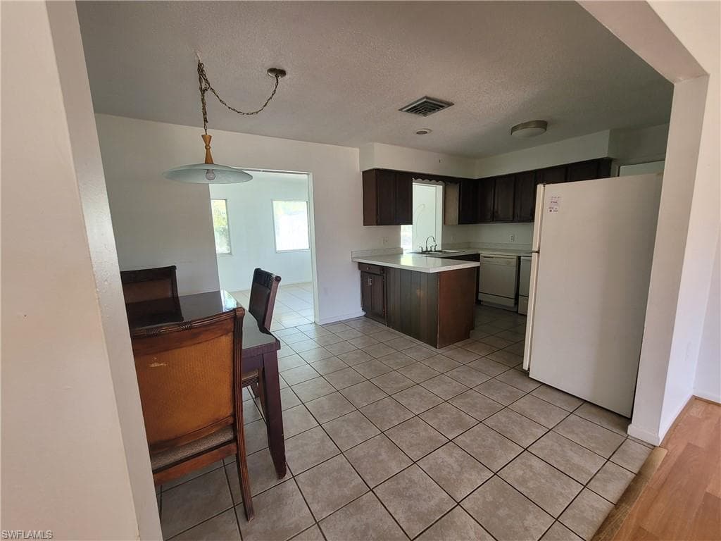 Kitchen featuring light countertops, white appliances, a peninsula, light tile patterned floors, and decorative light fixtures
