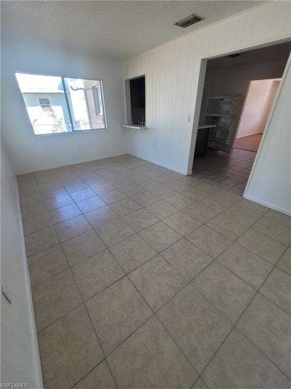 Spare room featuring light tile patterned floors, a textured ceiling, and wood walls