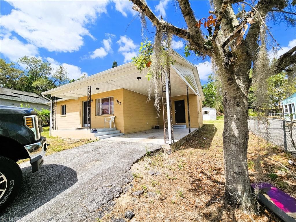 Rear view of house with an attached carport, driveway, a shed, and a patio
