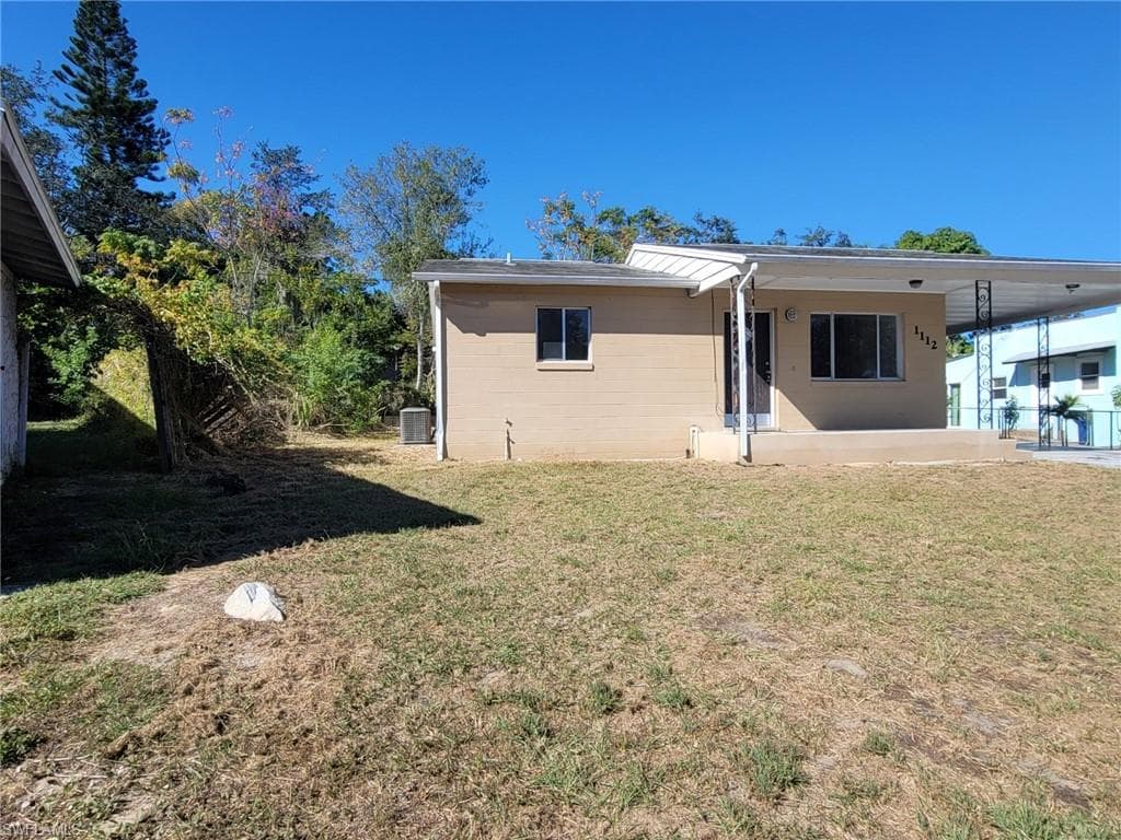 Back of property with a lawn, a patio area, and a carport