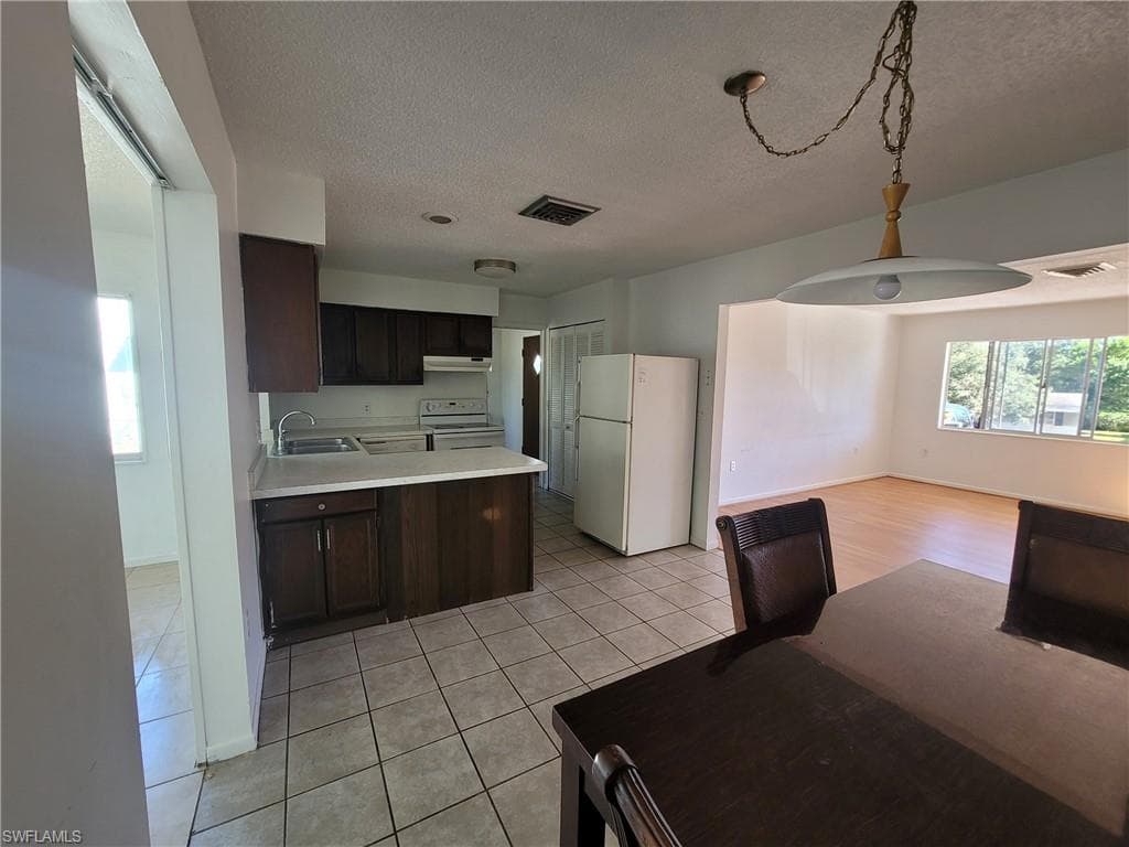 Kitchen featuring dark wood finish cabinetry, light countertops, a peninsula, white appliances, and a textured ceiling