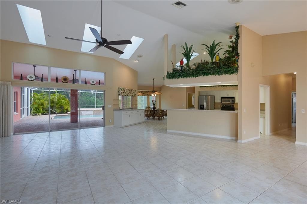 Unfurnished living room with high vaulted ceiling, a skylight, light tile patterned floors, and baseboards