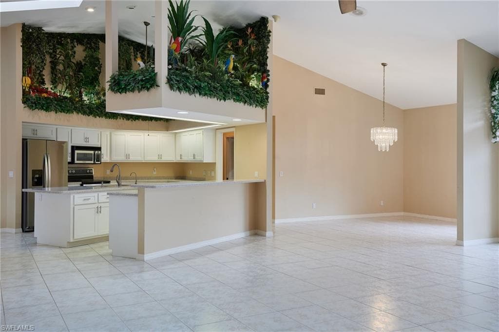 Kitchen with stainless steel appliances, high vaulted ceiling, light tile patterned floors, light countertops, and a chandelier