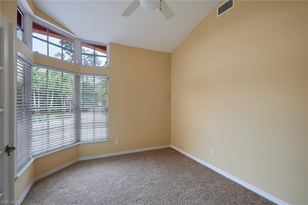 Carpeted empty room with a ceiling fan, baseboards, and lofted ceiling