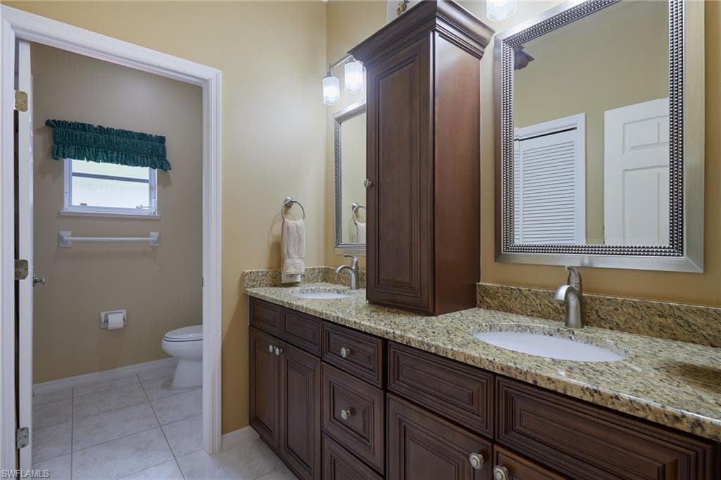 Bathroom with double vanity, toilet, tile patterned flooring, and baseboards