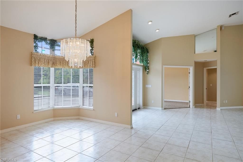 Unfurnished dining area featuring high vaulted ceiling, a chandelier, light tile patterned flooring, and baseboards