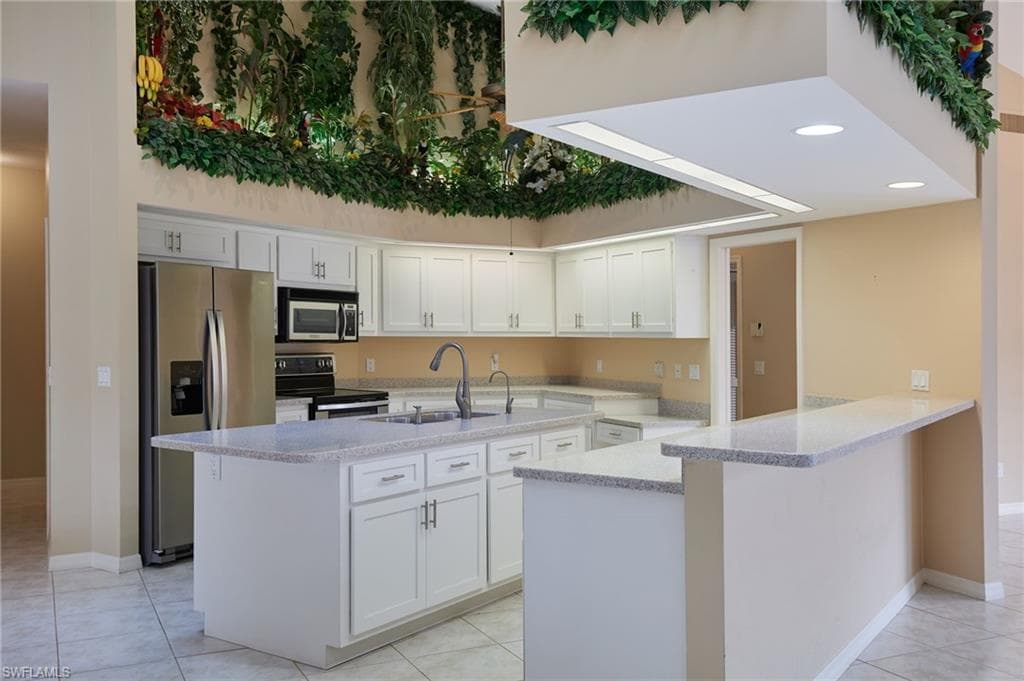 Kitchen featuring appliances with stainless steel finishes, a sink, a peninsula, white cabinetry, and light tile patterned floors