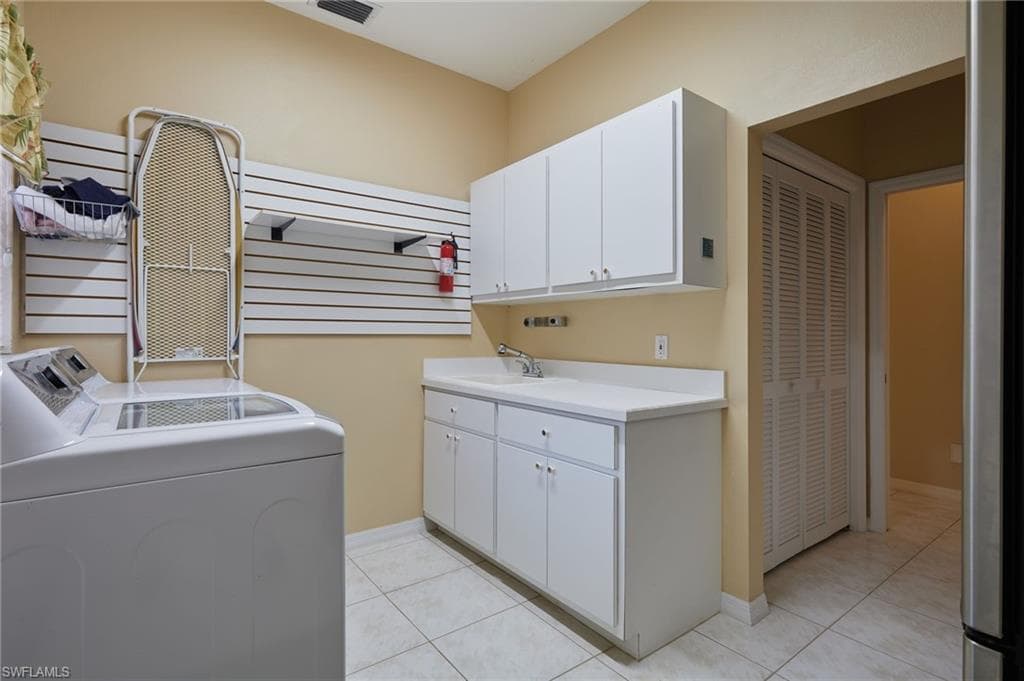 Laundry room featuring washing machine and dryer, cabinet space, light tile patterned flooring, and baseboards