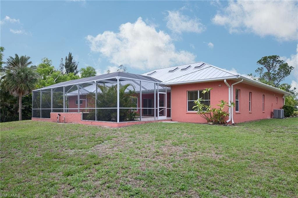 Back of property with central AC, a lawn, stucco siding, and a lanai