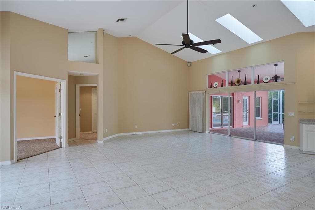 Spare room featuring high vaulted ceiling, light tile patterned flooring, a skylight, ceiling fan, and baseboards