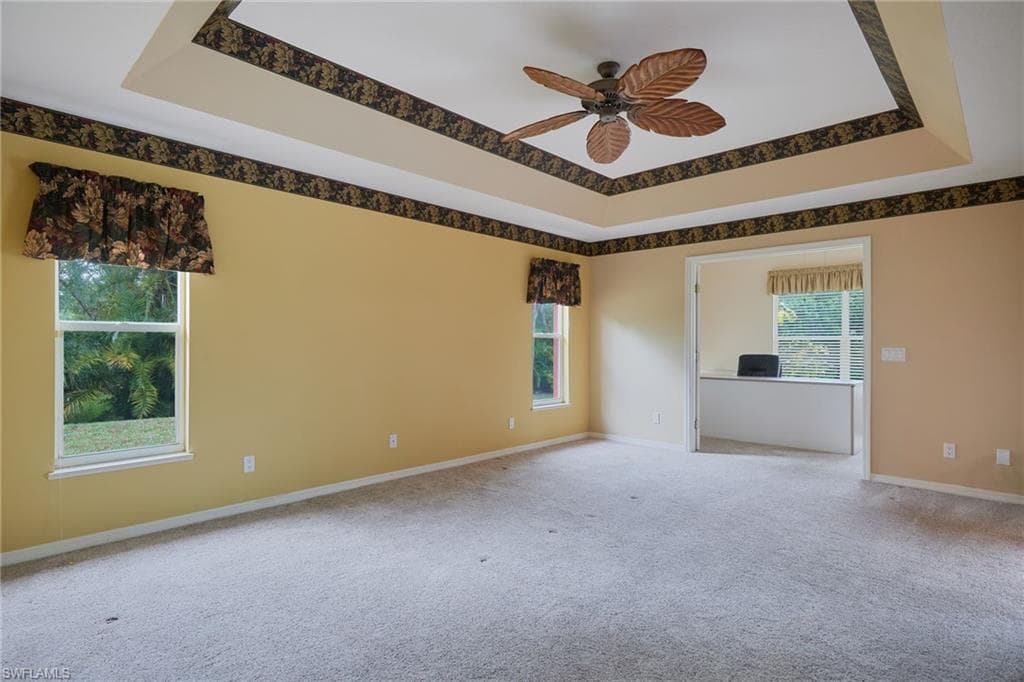 Carpeted spare room with ceiling fan, baseboards, and a tray ceiling