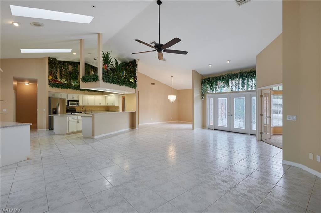 Unfurnished living room featuring high vaulted ceiling, light tile patterned floors, ceiling fan, baseboards, and a skylight