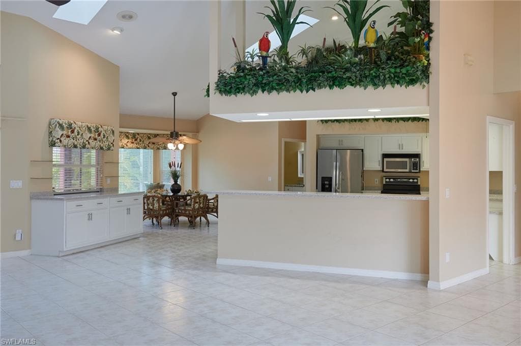 Kitchen featuring appliances with stainless steel finishes, high vaulted ceiling, a skylight, light tile patterned flooring, and decorative light fixtures