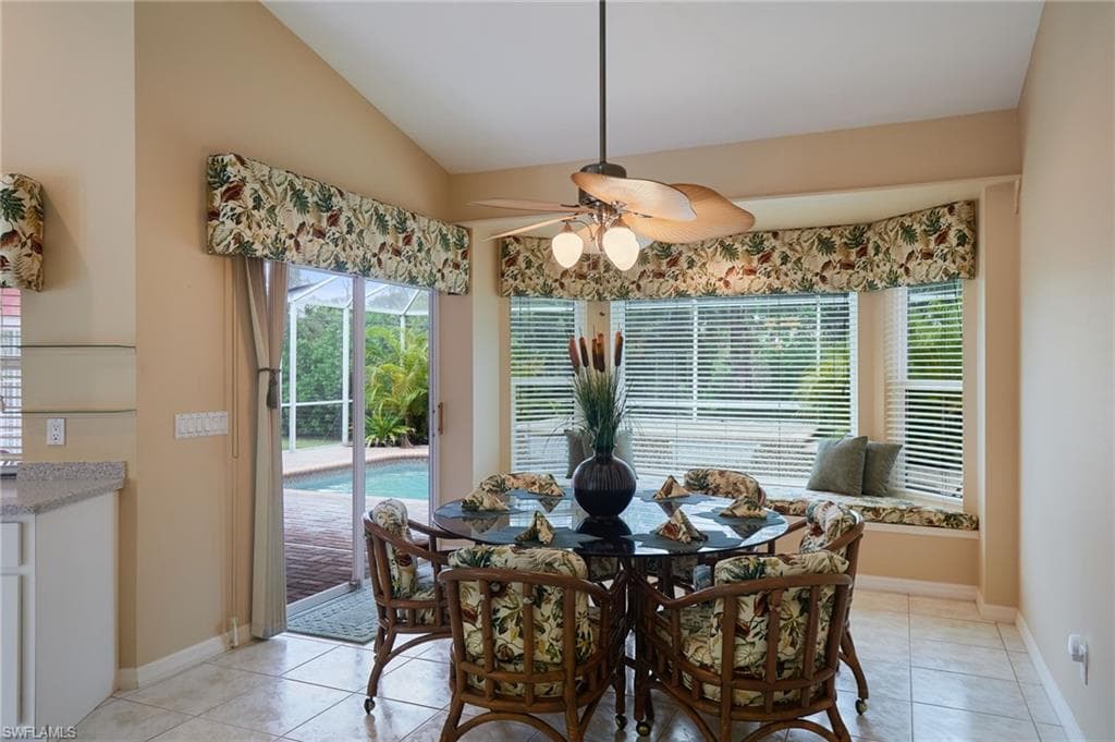 Dining area with ceiling fan, light tile patterned floors, vaulted ceiling, and baseboards