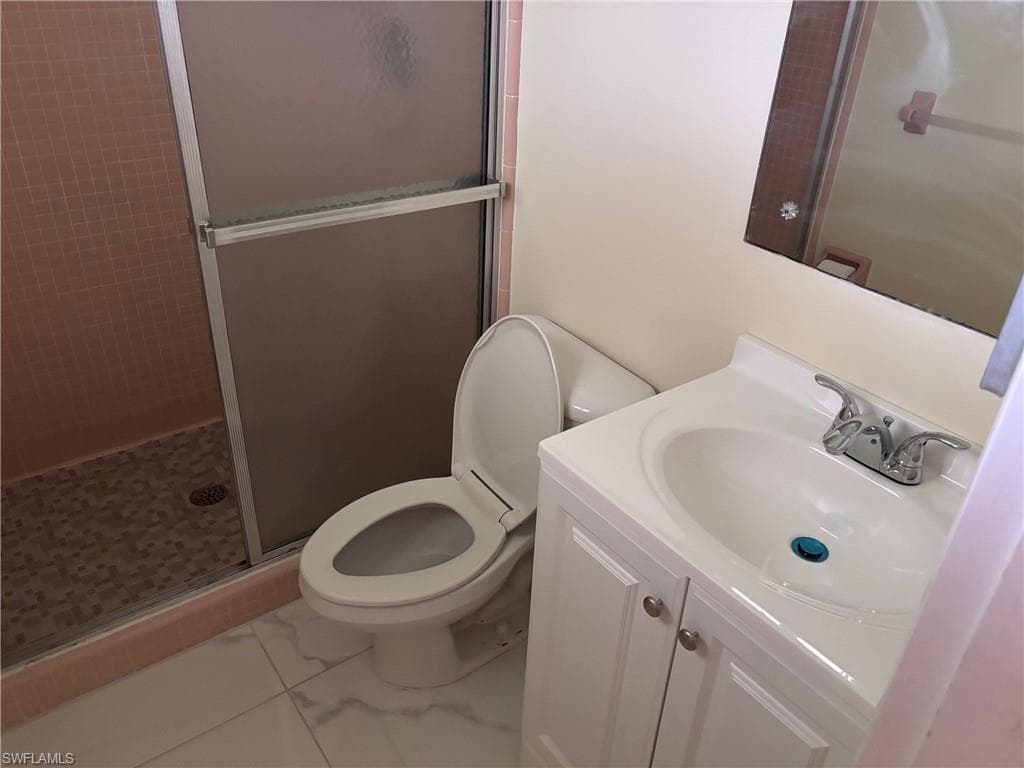 Full bathroom with a shower stall, marble finish floors, toilet, and vanity