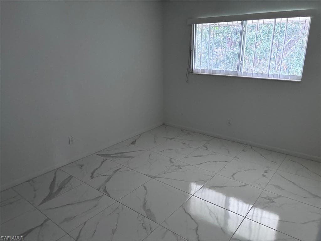 Empty room featuring marble look tiles and baseboards