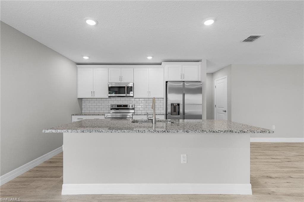 Kitchen featuring appliances with stainless steel finishes, a sink, a kitchen island with sink, baseboards, and light wood finished floors