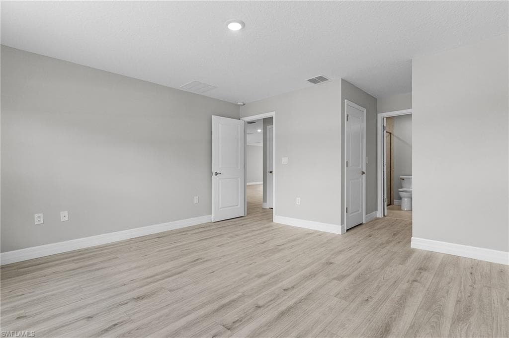Unfurnished bedroom with light wood-style floors, baseboards, recessed lighting, and connected bathroom