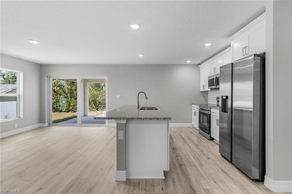 Kitchen with stainless steel appliances, a sink, a center island with sink, stone countertops, and light wood-style floors