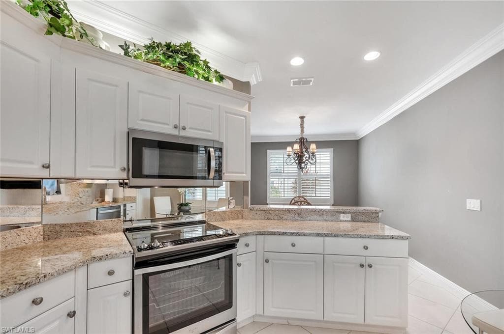 Kitchen featuring stainless steel appliances, a peninsula, crown molding, white cabinetry, and a chandelier