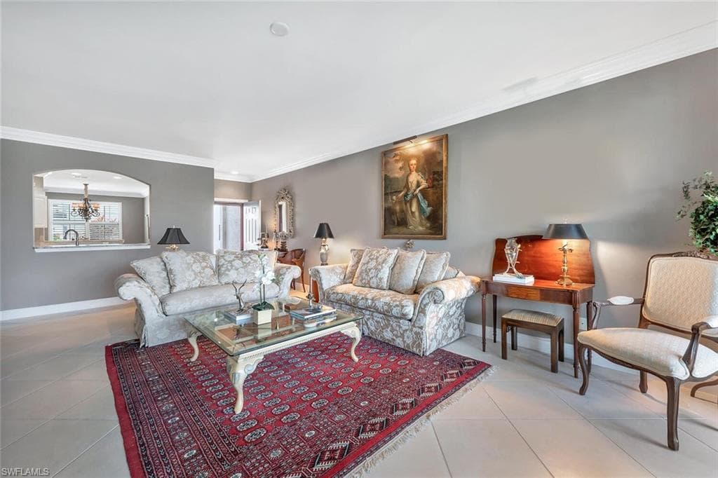Living room featuring tile patterned floors, ornamental molding, baseboards, arched walkways, and a chandelier