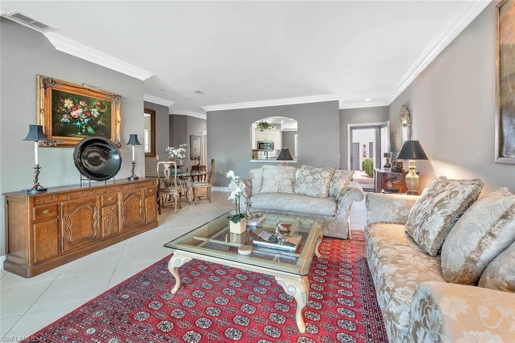 Living area featuring light tile patterned floors, crown molding, arched walkways, and baseboards