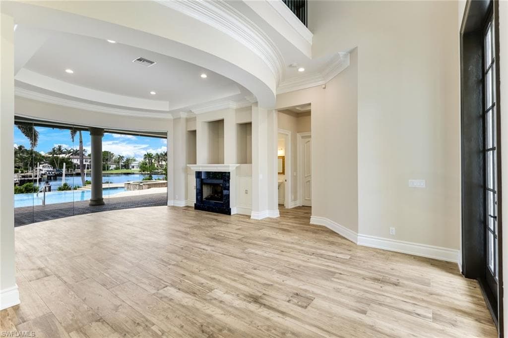 Foyer leading in to Fomal Living Room with gas fireplace, midered glass floor to ceiling windows, ornamental molding, light wood-style floors, a raised ceiling, and a fireplace. Impressive view of gorgeous pool extensive water views of the bay.