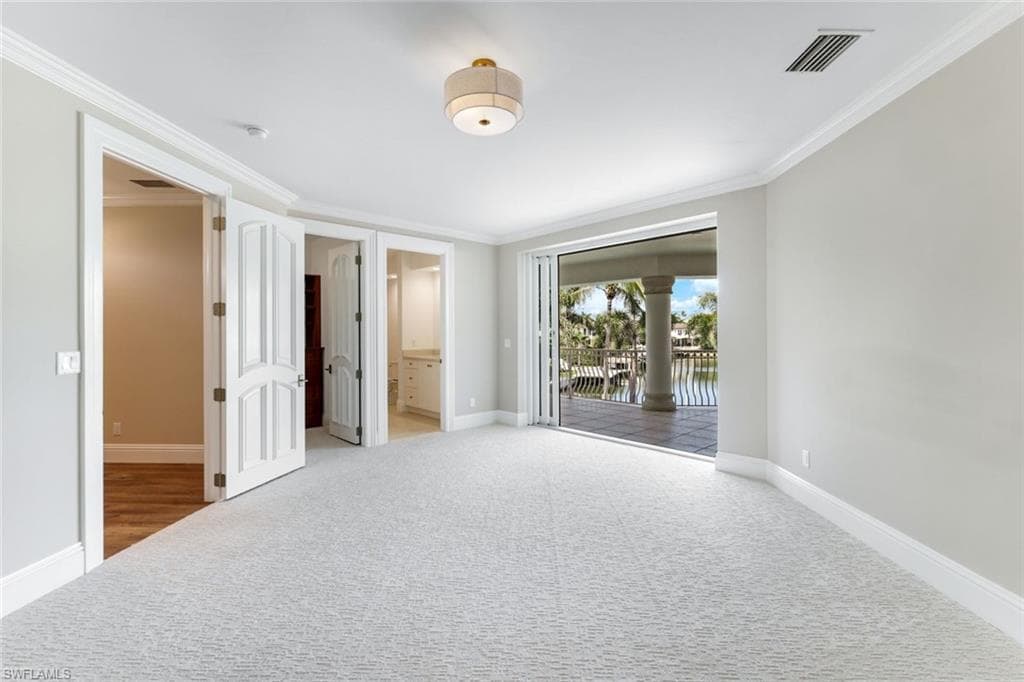 Upstairs bedroom #3 with ornate columns, ornamental molding, lush fresh carpet, walk in closet and wrap around balcony overlooking the pool area, dock and bay.