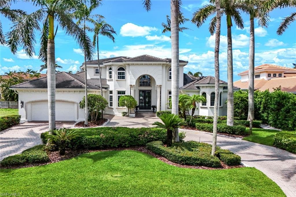 View of front of property featuring circular decorative driveway, a front yard, stucco siding, french doors, and oversized 3 car attached garage.